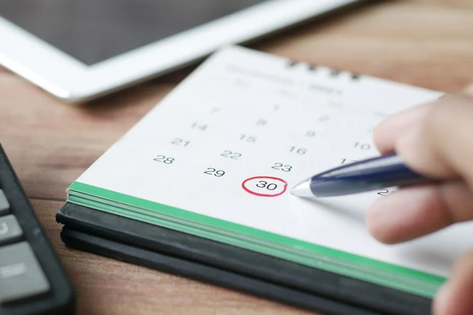 Person marking a payday date on a desk calendar